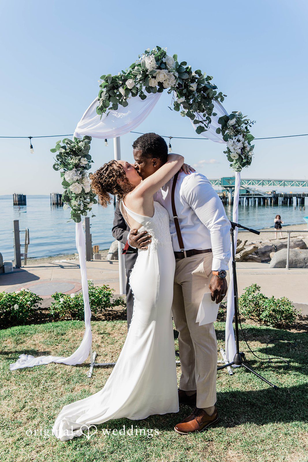 Naomi + Darrell Bride and groom sharing a kiss under a floral arch.