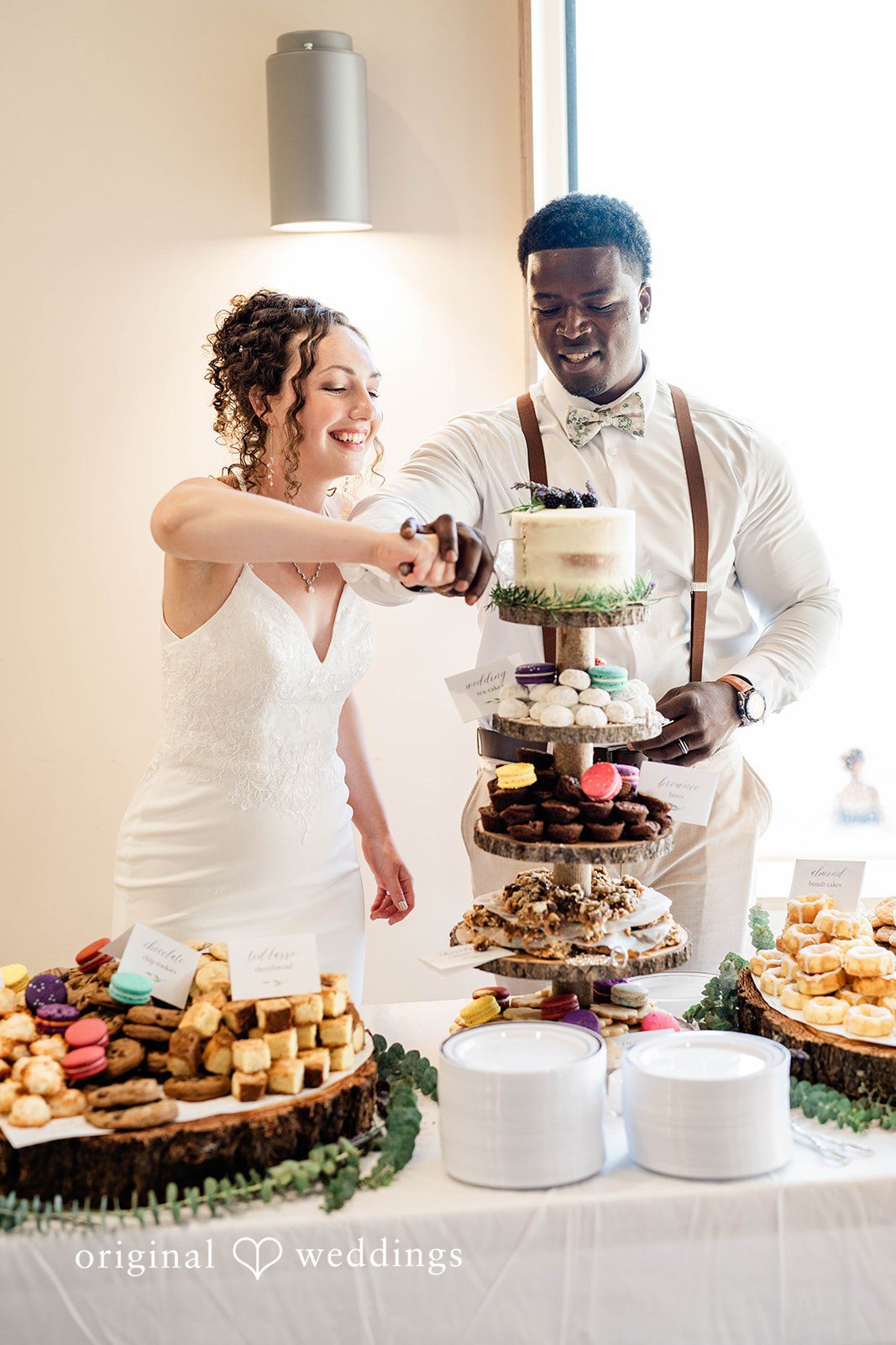 Naomi + Darrell Bride and groom cutting their wedding cake together at a dessert table.