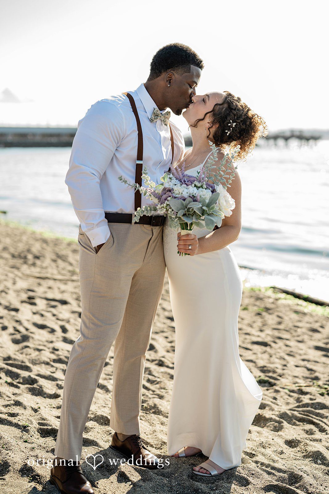 Naomi + Darrell Groom holding the bride close while standing on a beach.