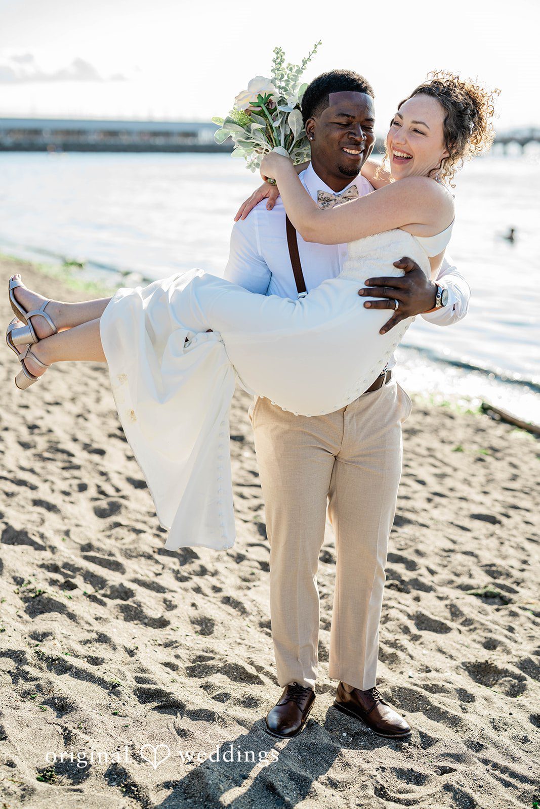 Naomi + Darrell Groom carrying the bride in his arms along the beach.