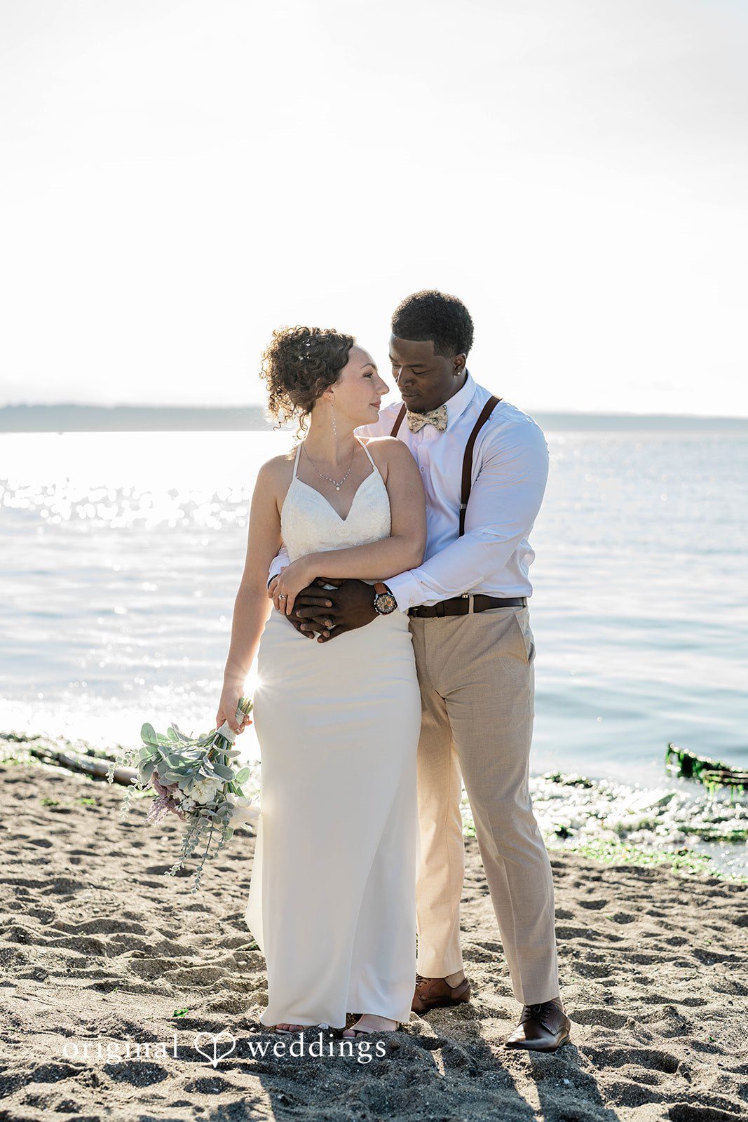Naomi + Darrell Newlyweds standing together and holding hands on a sandy shore.