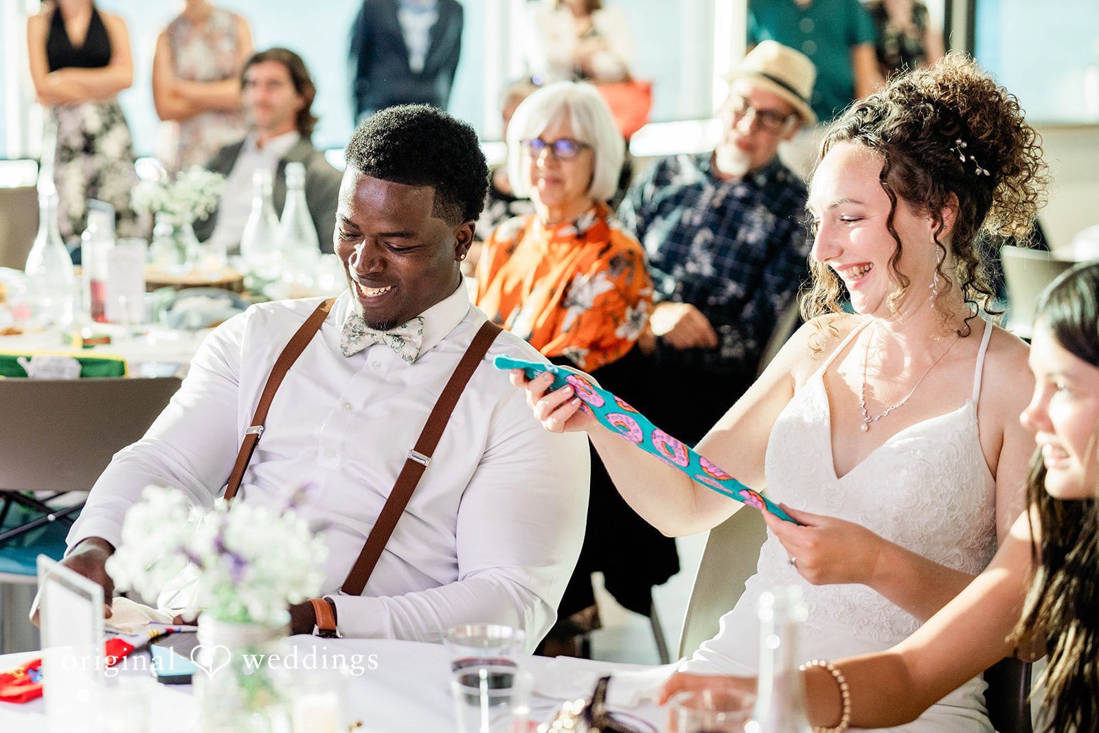 Naomi + Darrell Groom laughing while seated with his bride and guests at a reception table.