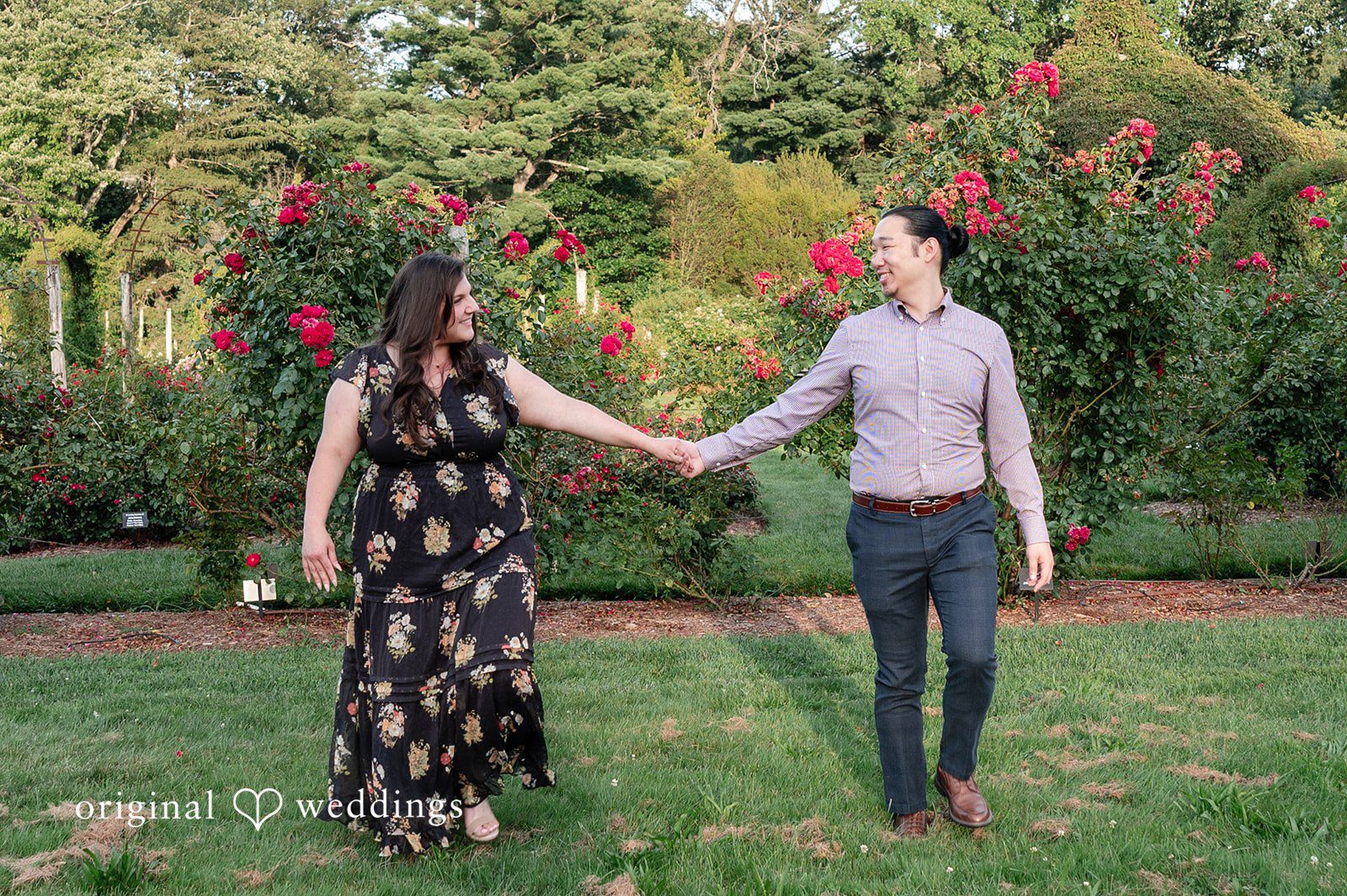Gabrielle + James A couple walking hand-in-hand along a garden path, with the woman wearing a long dark floral dress.
