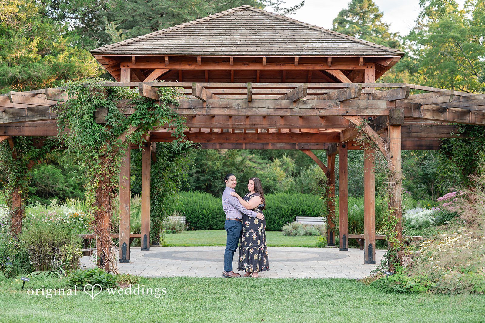 Gabrielle + James A couple standing together inside a large wooden garden gazebo.