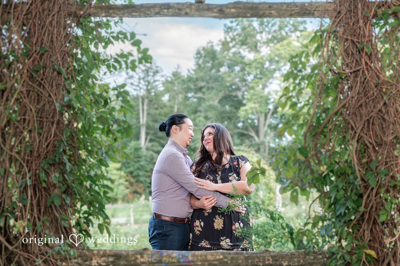 Gabrielle + James A couple standing together framed between two tall brick pillars covered in ivy.