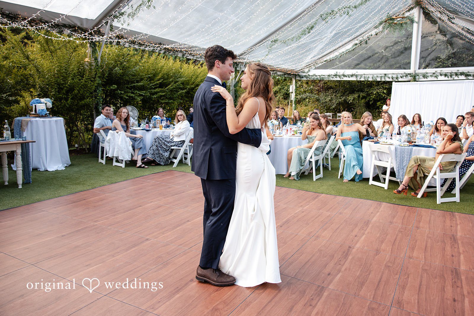 Alissa + Duncan A bride and groom dancing together on a wooden dance floor surrounded by reception guests.