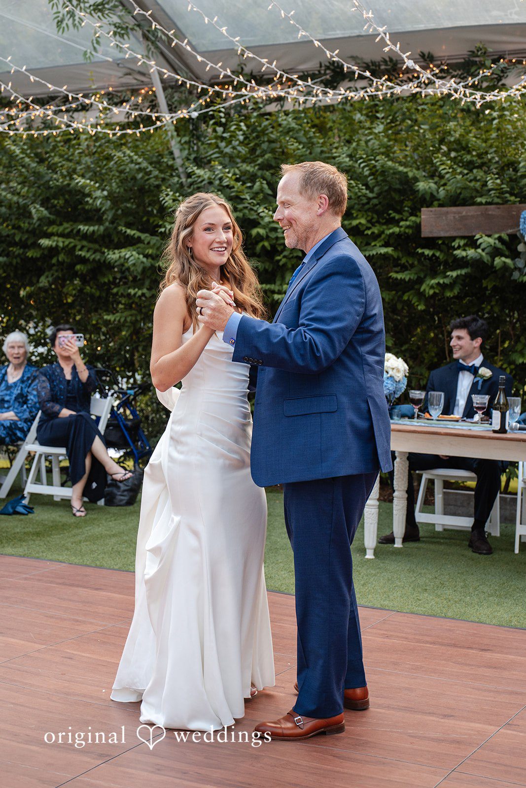 Alissa + Duncan A bride in her white gown dancing with a man in a blue suit on a dance floor.