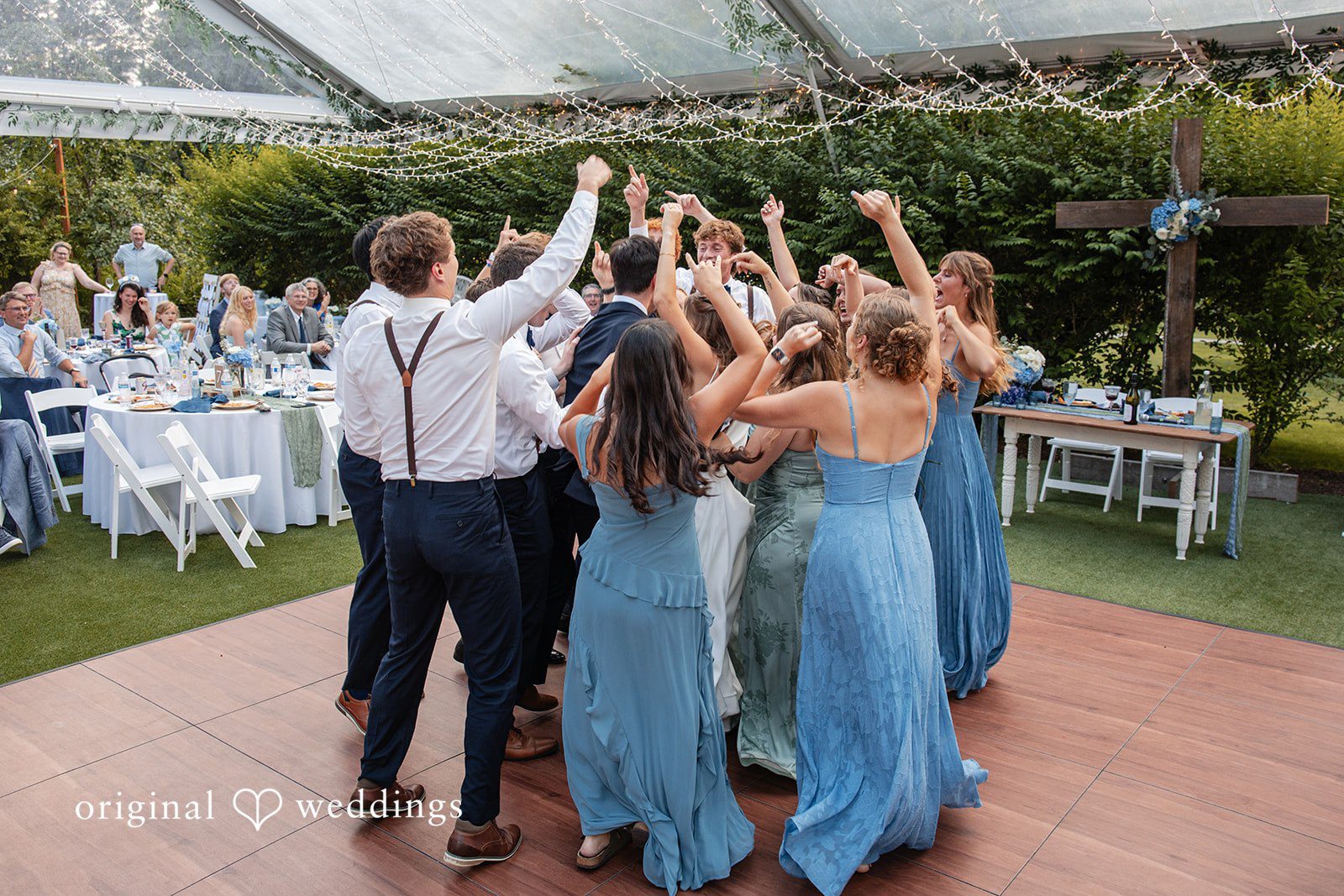 Alissa + Duncan A wedding party cheering and dancing together with raised hands on a dance floor.