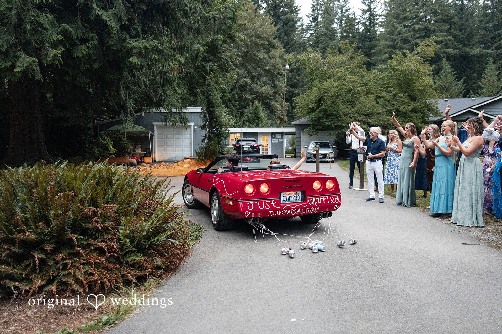 Alissa + Duncan A red convertible car driving away down a road lined with waving wedding guests.