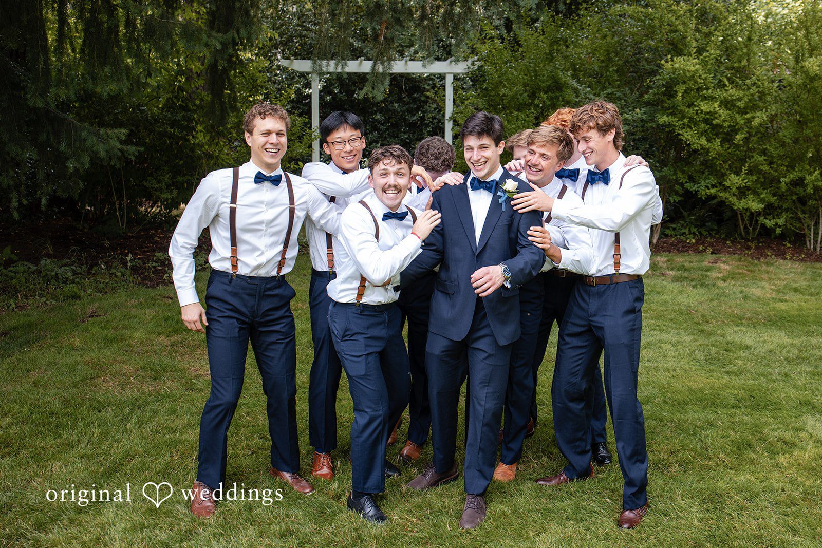 Alissa + Duncan A groom posing with his groomsmen wearing white shirts, suspenders, and blue bow ties.