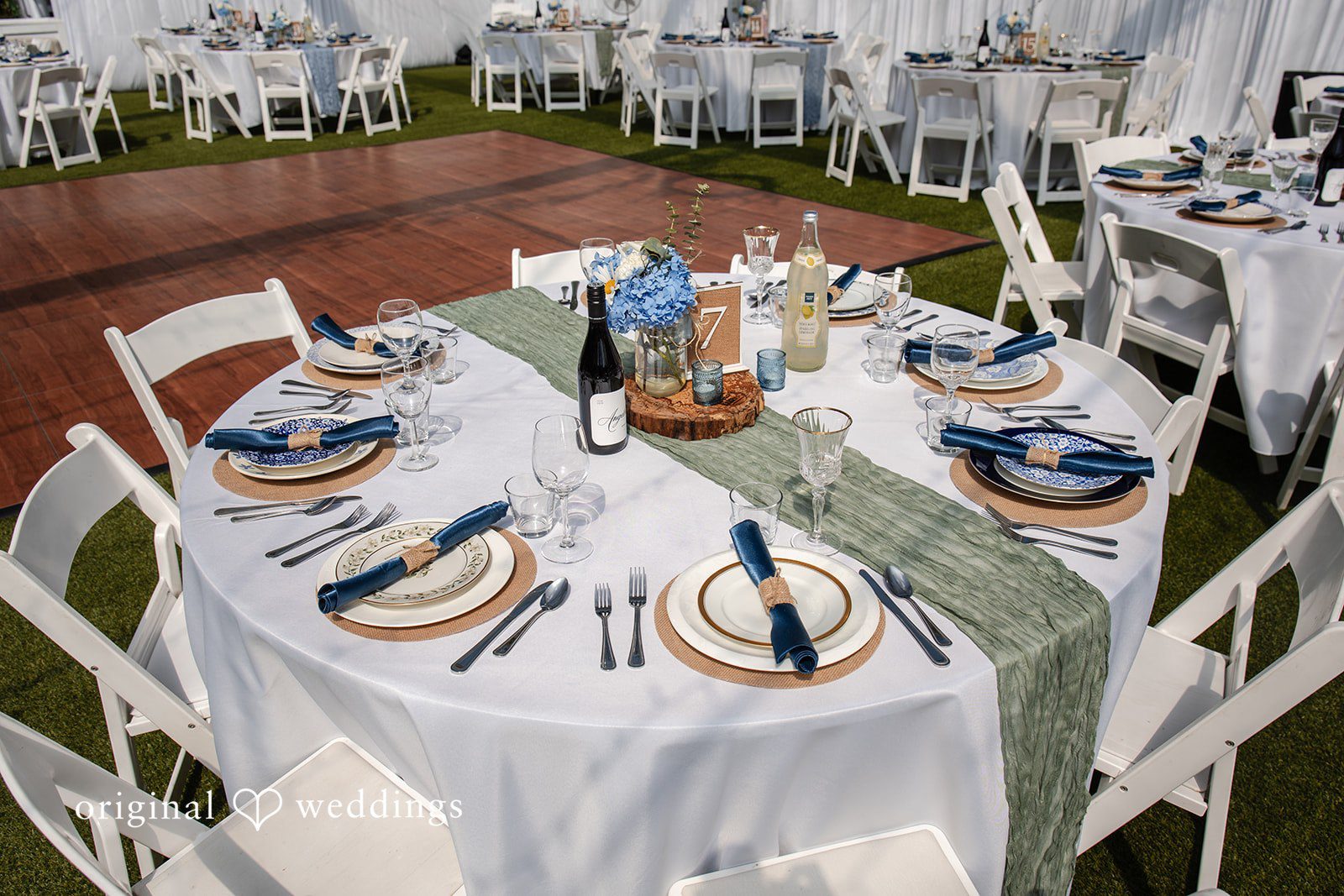 Alissa + Duncan A round dinner table set with plates, glassware, and blue accents for a wedding.