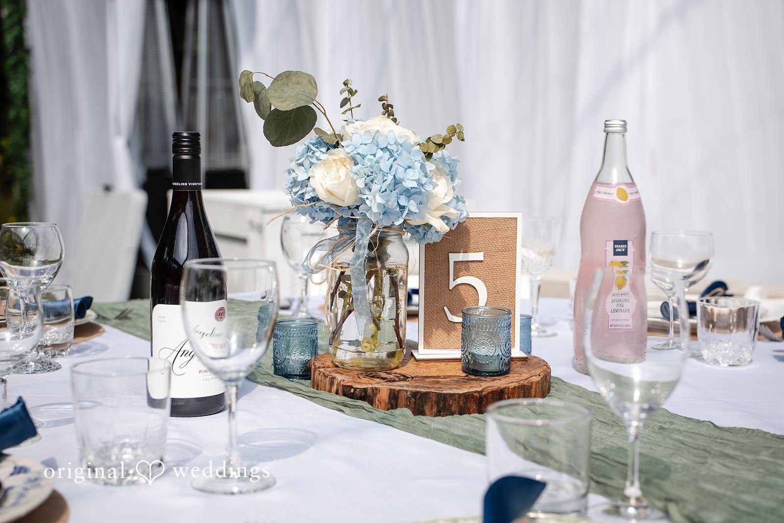 Alissa + Duncan A wedding table centerpiece featuring blue flowers, candles, and glassware.