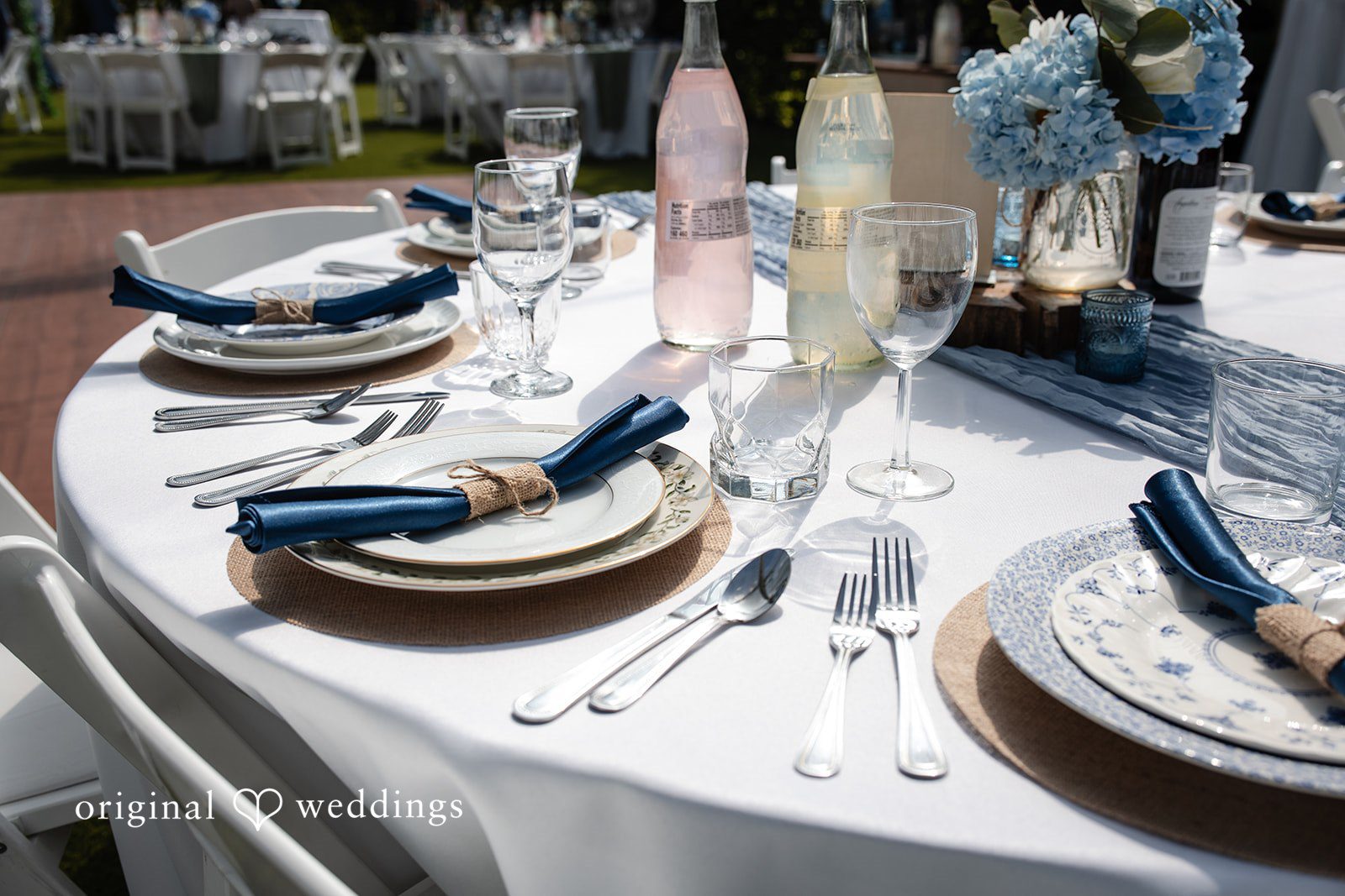 Alissa + Duncan A close-up of a wedding table setting with stacked plates, cutlery, and a blue napkin.