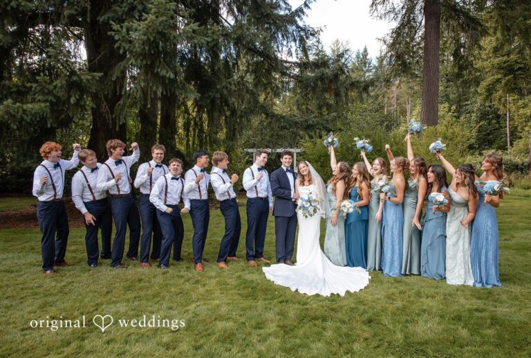 A full wedding party posing together with bridesmaids in light blue and groomsmen in dark suits at Evergreen Meadows by Seattle Wedding Photographers from Original Weddings..