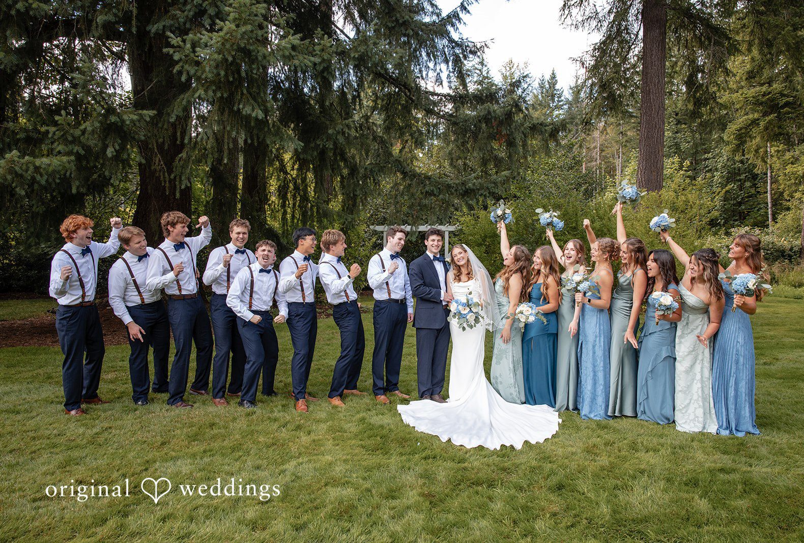 A full wedding party posing together with bridesmaids in light blue and groomsmen in dark suits at Evergreen Meadows by Seattle Wedding Photographers from Original Weddings..