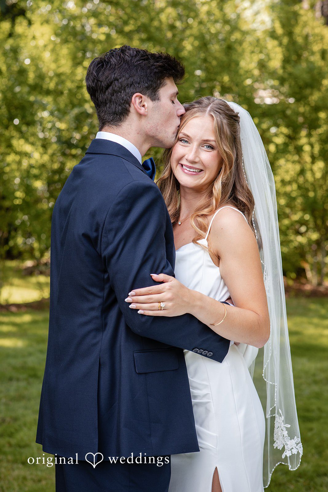 Alissa + Duncan A groom embracing his smiling bride from behind under her flowing veil.