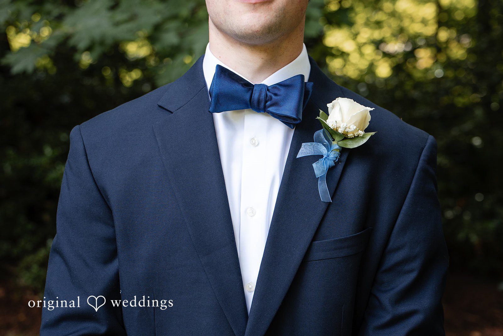 Alissa + Duncan A close-up of a groom wearing a dark blue suit with a bow tie and white boutonniere.