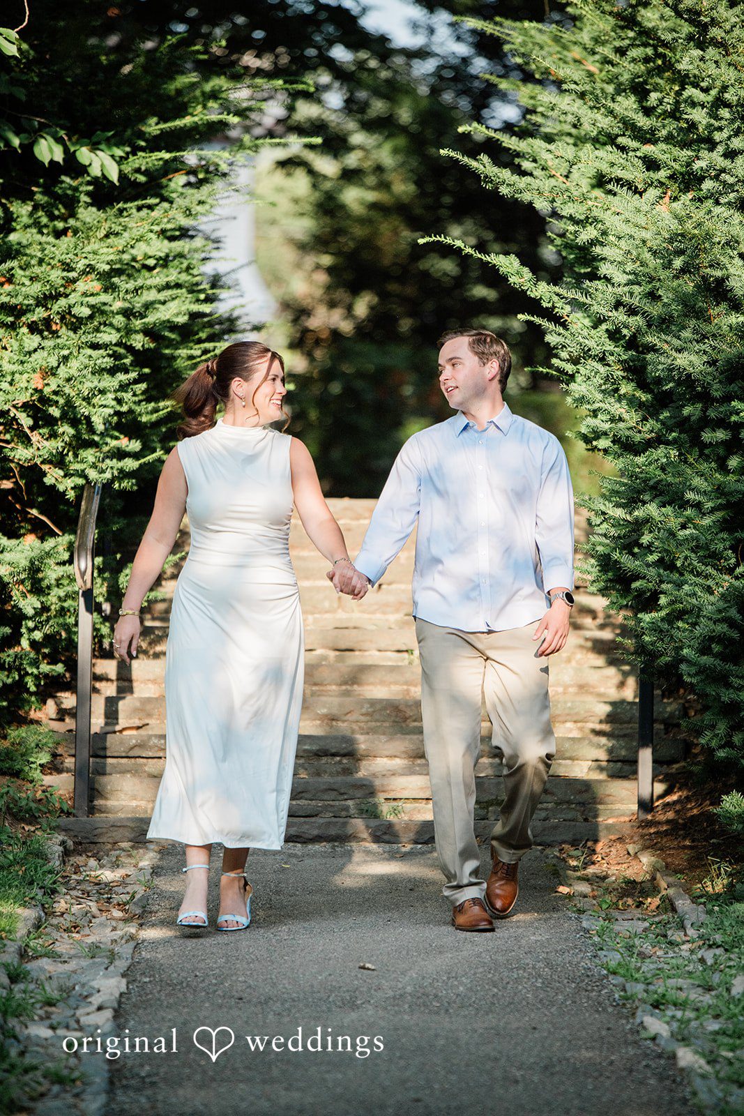 A couple walking hand-in-hand down a path surrounded by lush greenery.