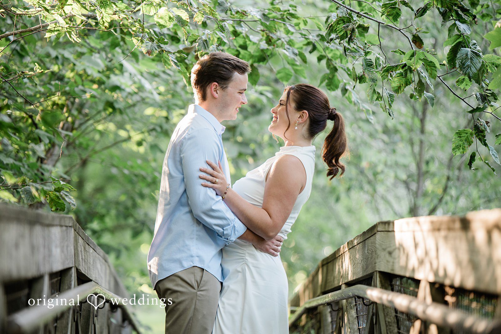 A man and a woman holding hands and looking at each other near a rustic fence.
