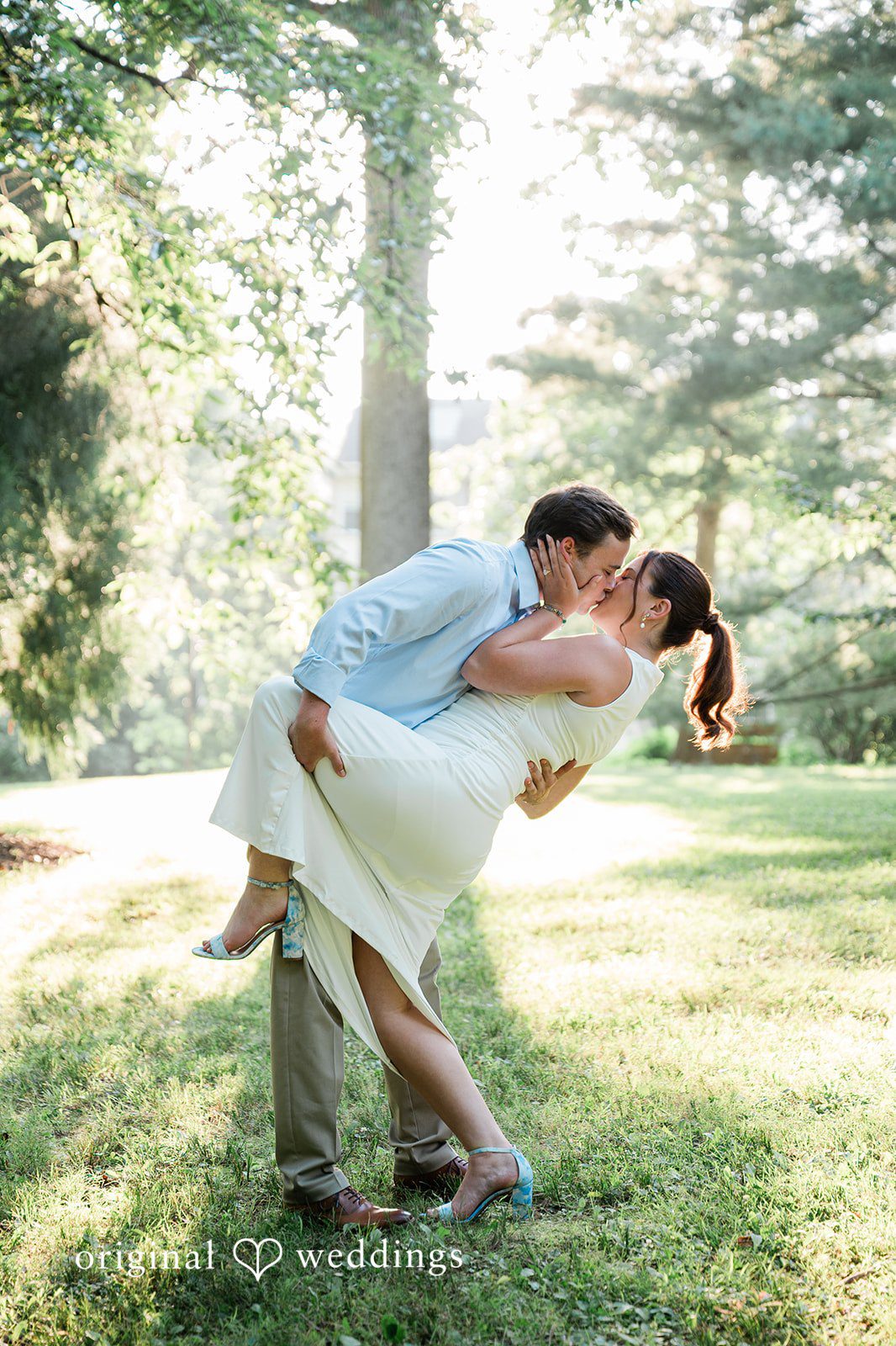 A man romantically dipping a woman backward in the middle of a grassy field.