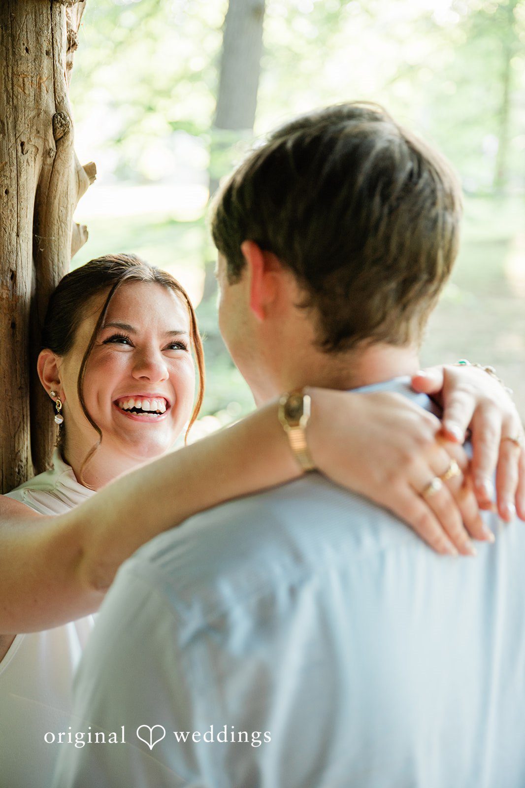A smiling woman wrapping her arms around a man's neck from behind.