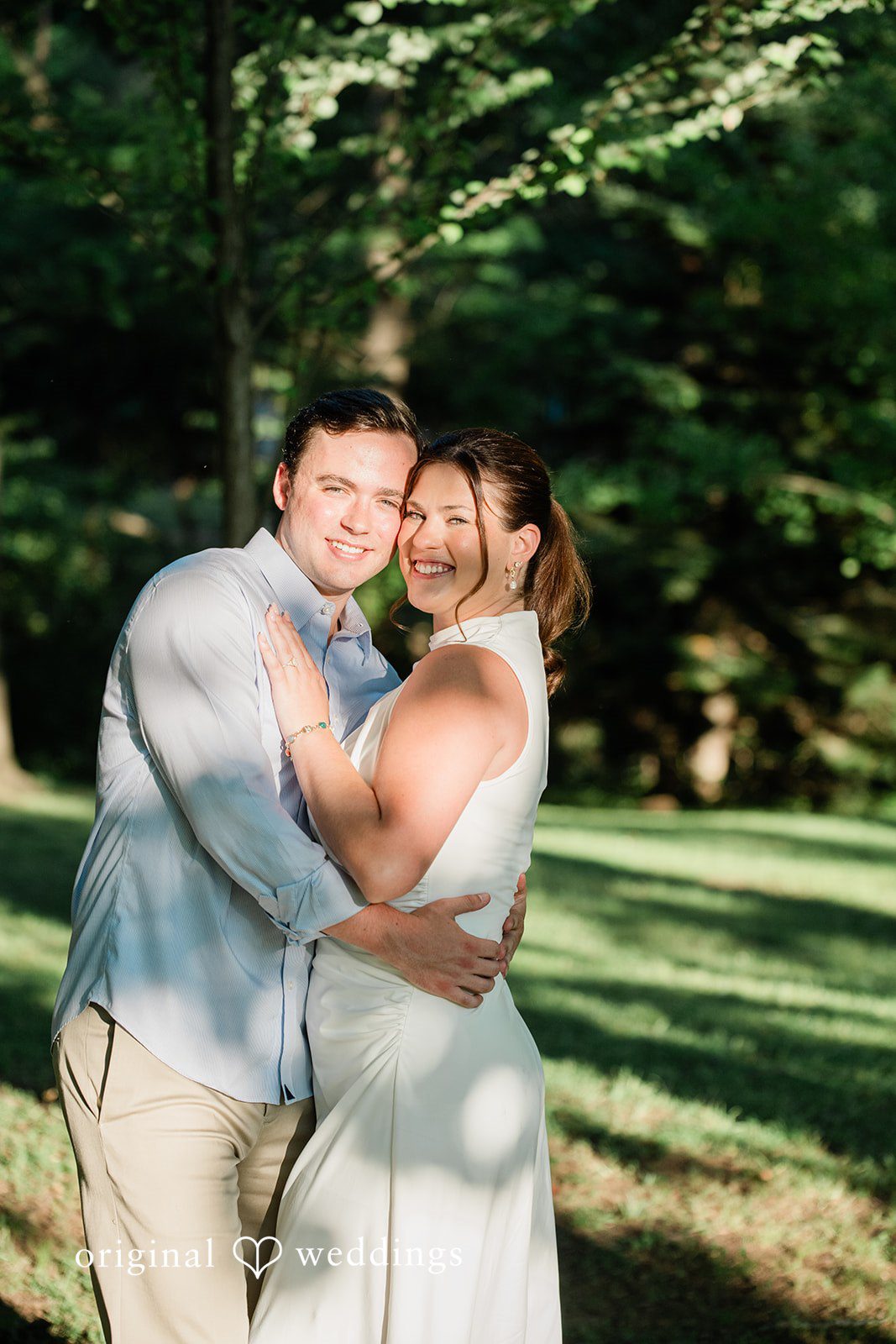 A couple sharing a close embrace while smiling near some trees.