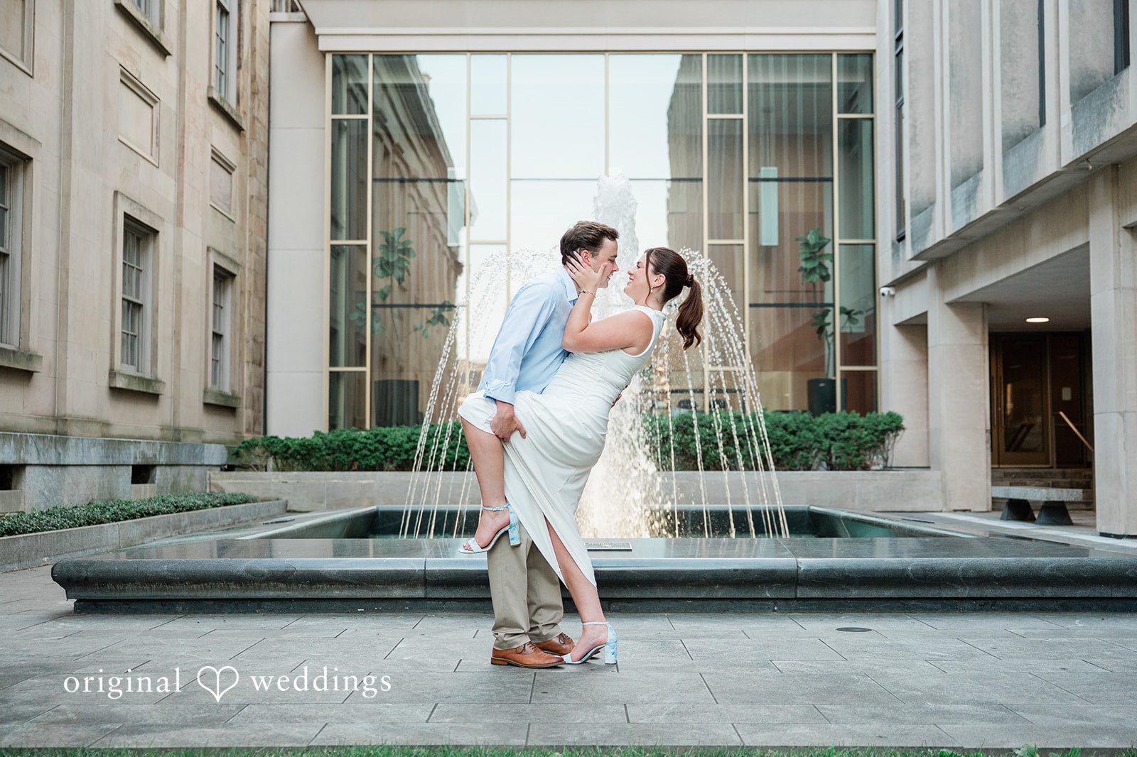 A couple posing near a modern building with a reflecting pool.