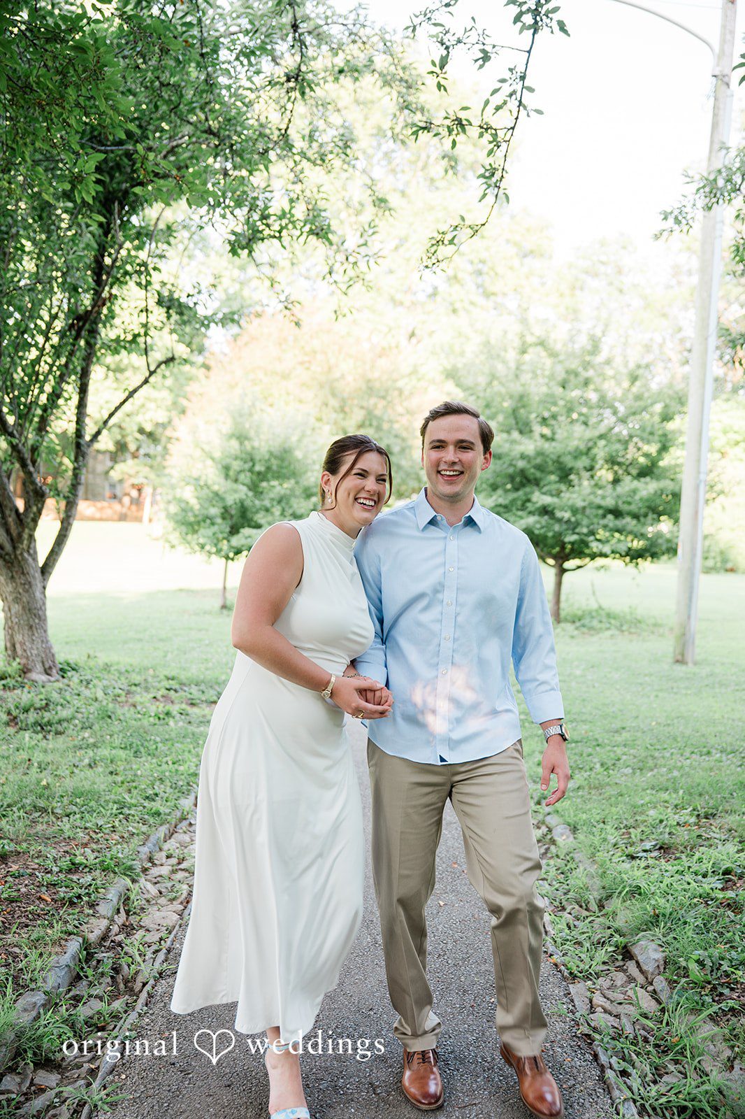 A couple posing together in a grassy clearing surrounded by trees.