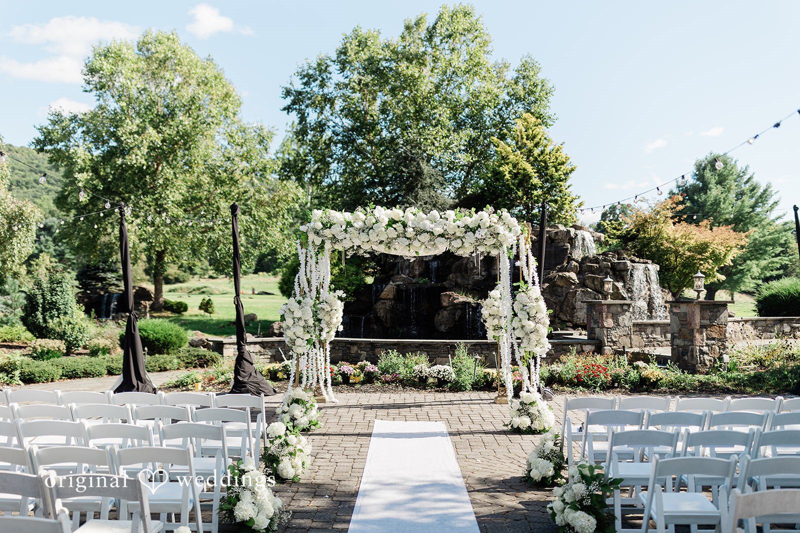 Julia + Camden An empty ceremony setup with a white runner leading to a flower-covered archway.