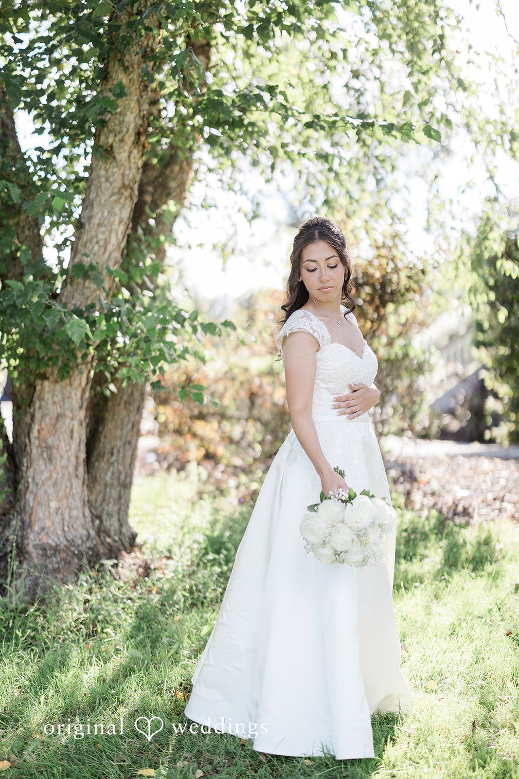 Julia + Camden A bride posing for a portrait in her white wedding dress on a grassy lawn.