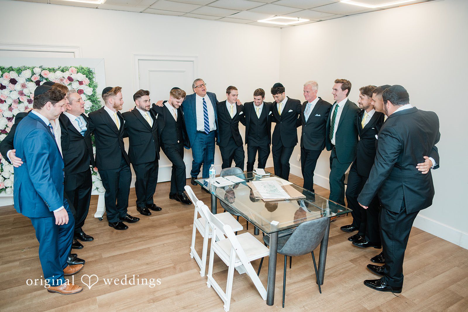 Julia + Camden A groom standing in a formal room surrounded by his groomsmen.