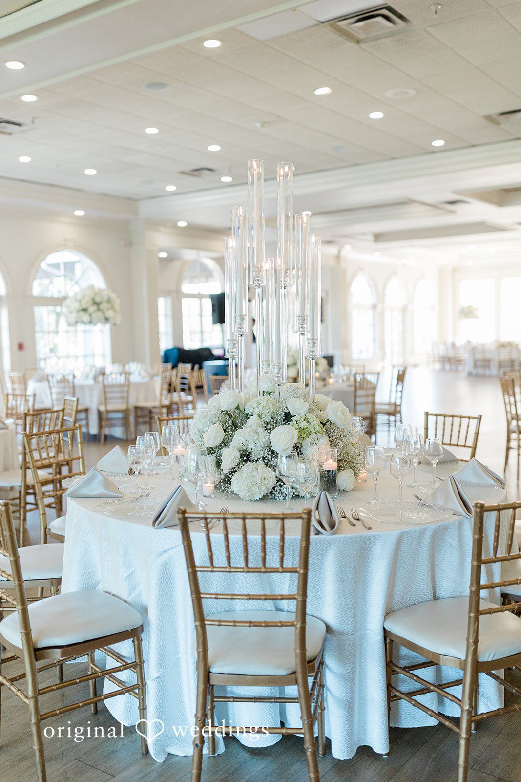 Julia + Camden A large round banquet table dressed in white linens and surrounded by wooden chairs.