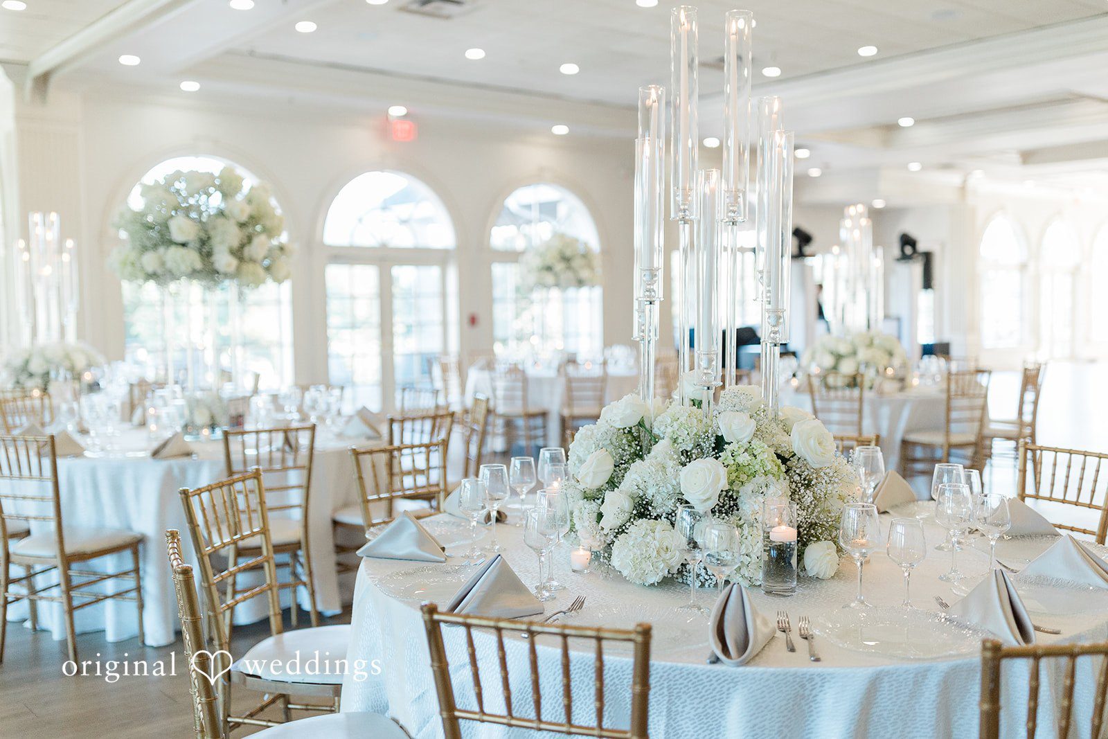 Julia + Camden A formal dining room setup featuring elegant tables and tall, white centerpieces.