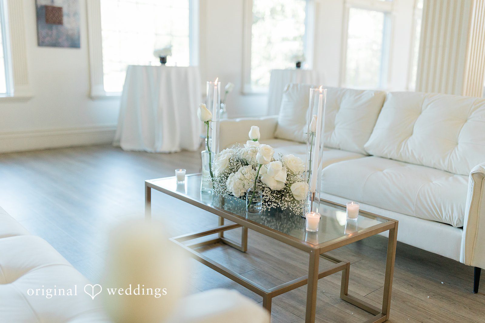 Julia + Camden A lounge area featuring light-colored sofas, a glass coffee table, and tall floral arrangements.