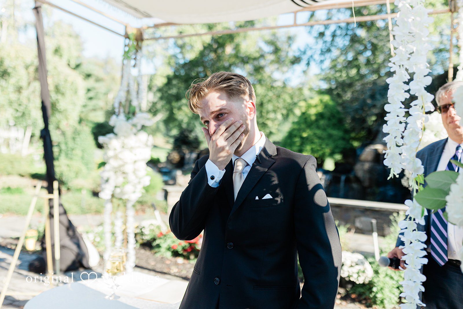Julia + Camden A groom in a black suit smiling while walking along a path.