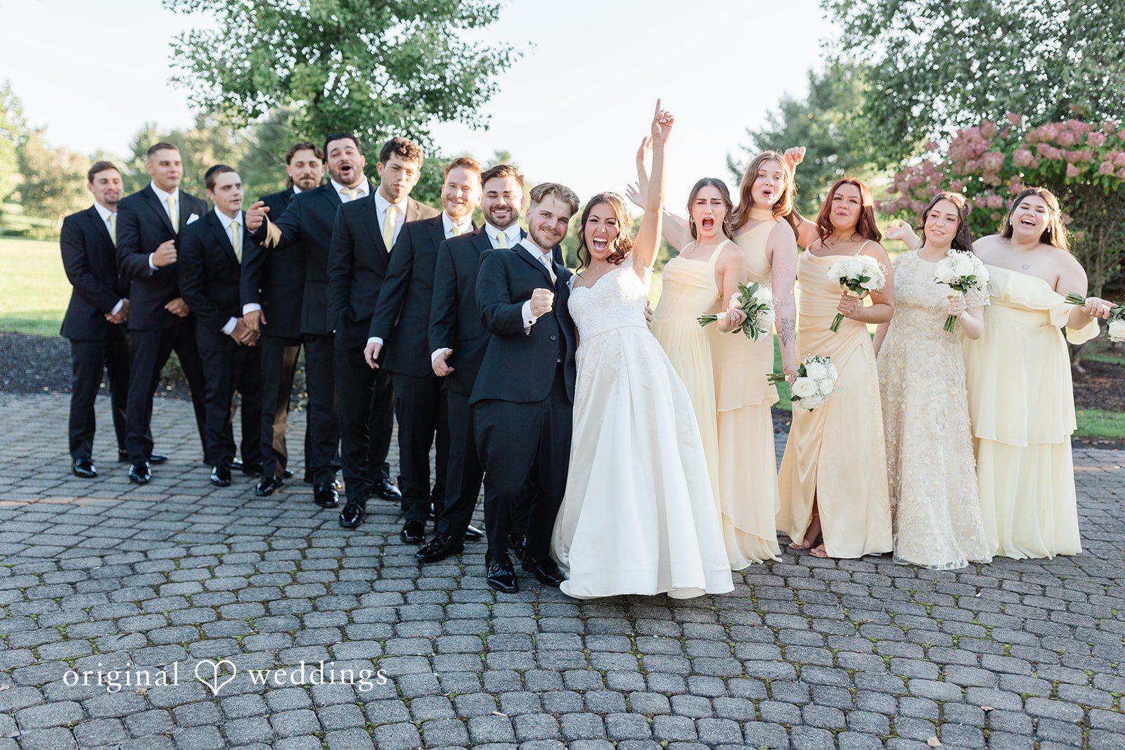 Julia + Camden A large wedding party poses together on a cobblestone courtyard area.