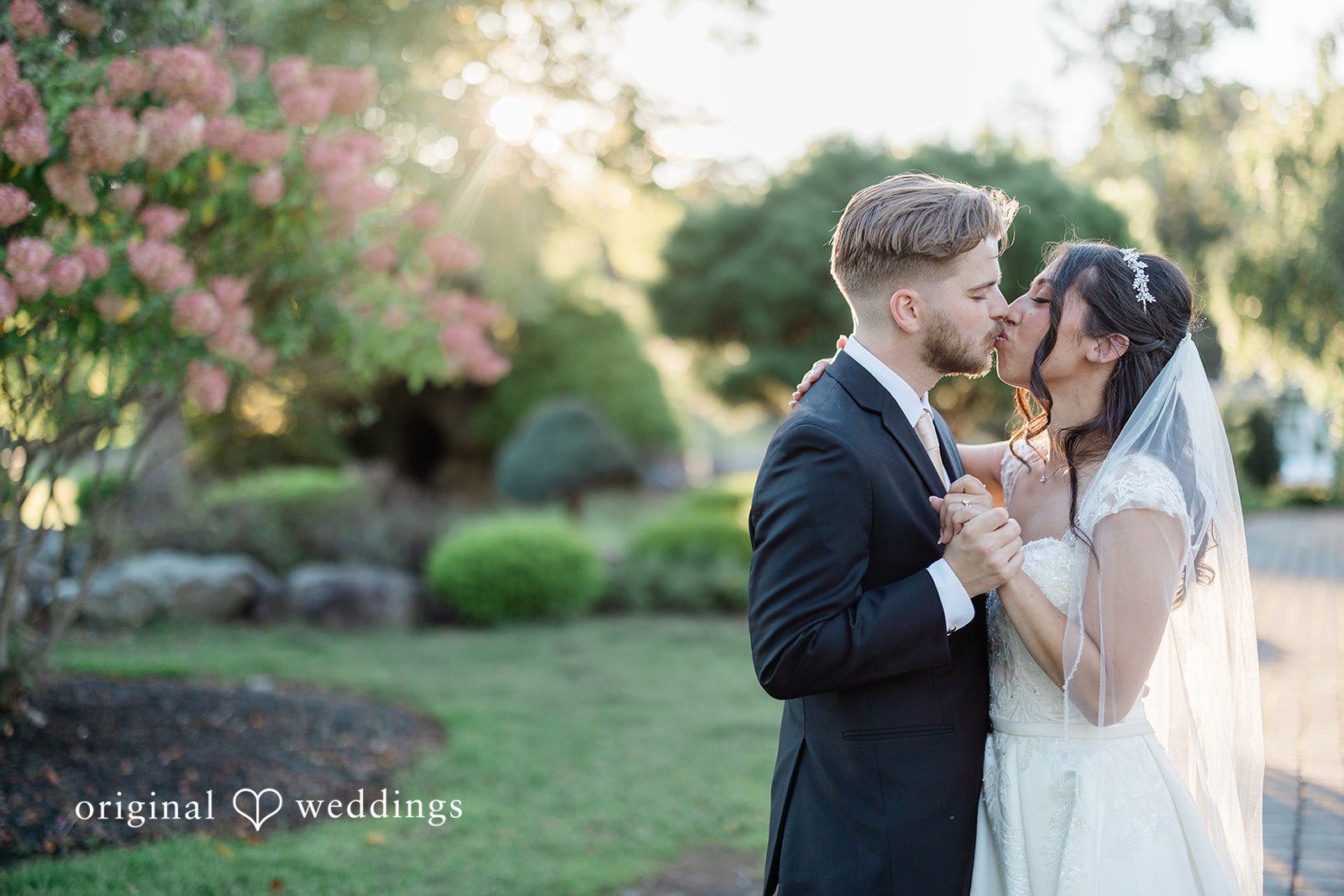 Julia + Camden A bride and groom share a close embrace on a grassy lawn with soft lighting.