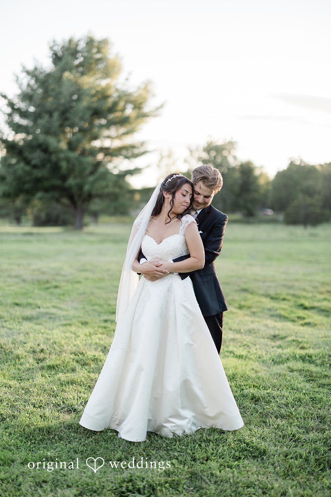 Julia + Camden A bride and groom standing together through a wide, open grassy field.