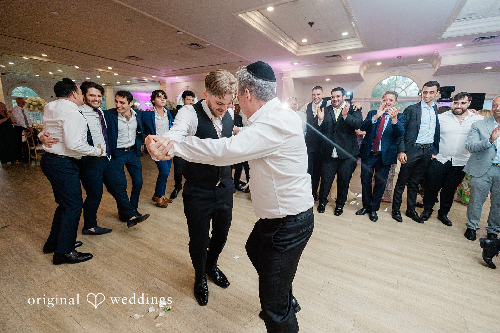 Julia + Camden A wedding guest and groom dance joyfully surrounded by cheering guests on a dance floor.