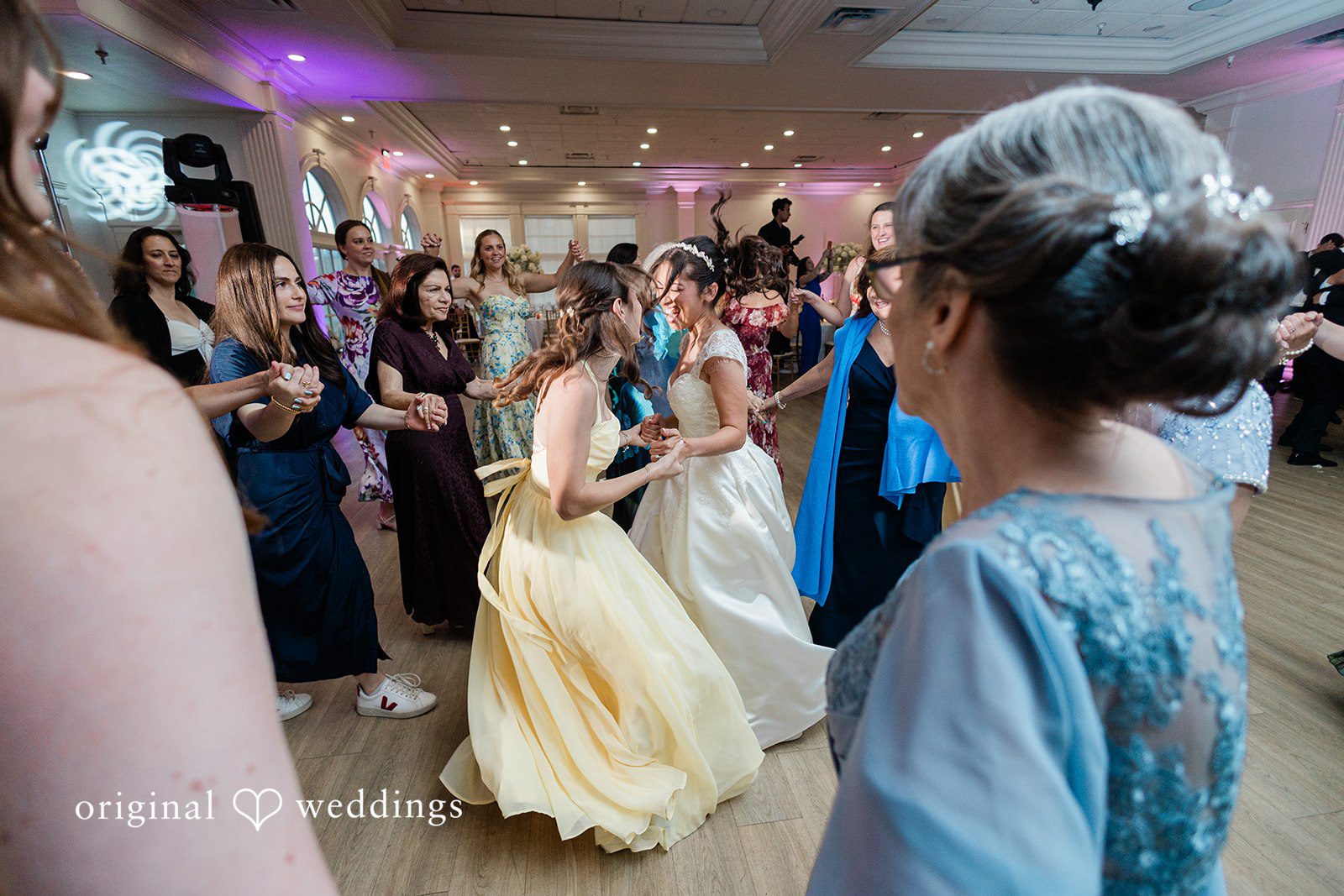 Julia + Camden Guests dance energetically under colorful lights at a reception party.