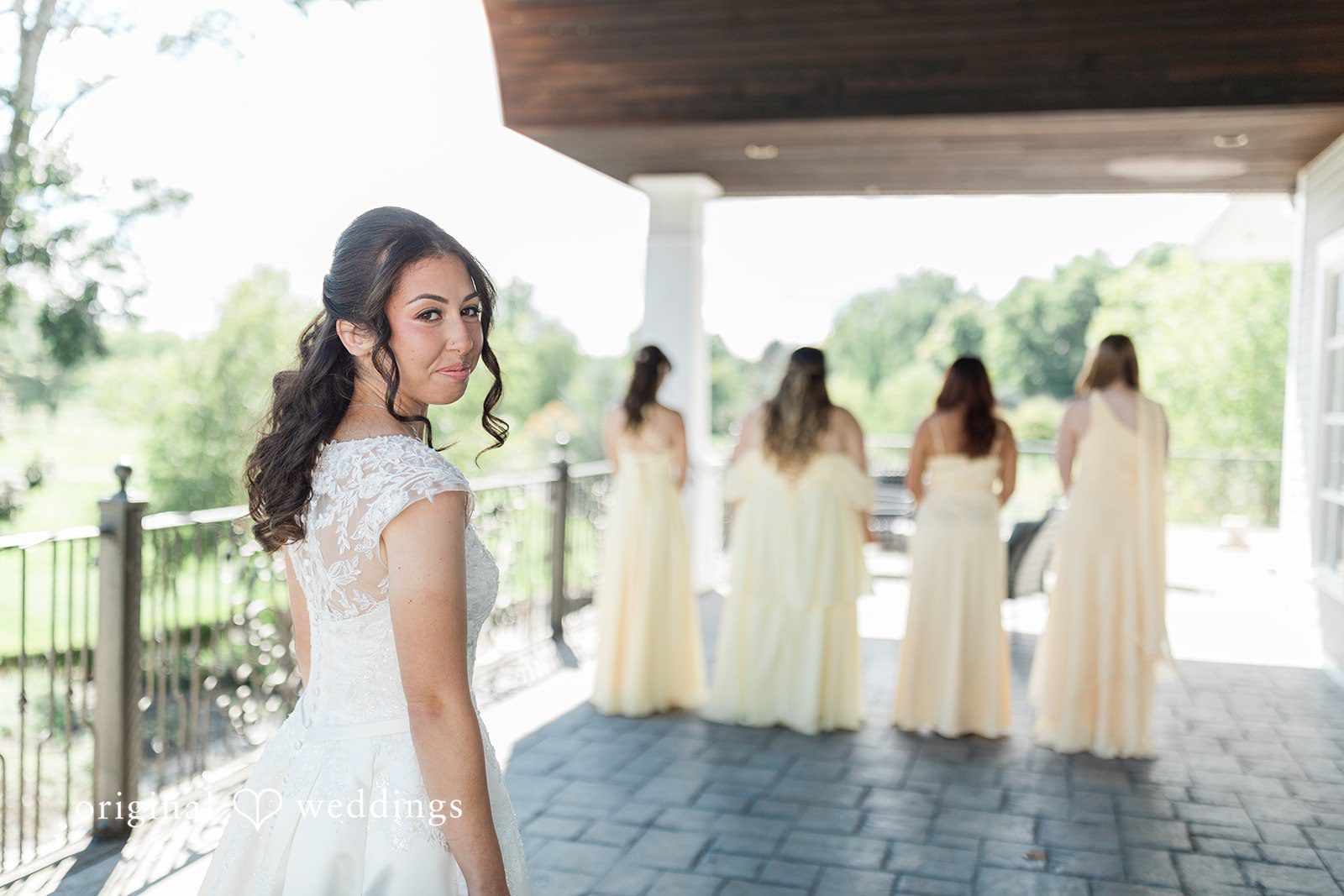 Julia + Camden A bride standing under an awning while a group of bridesmaids walks in the background.
