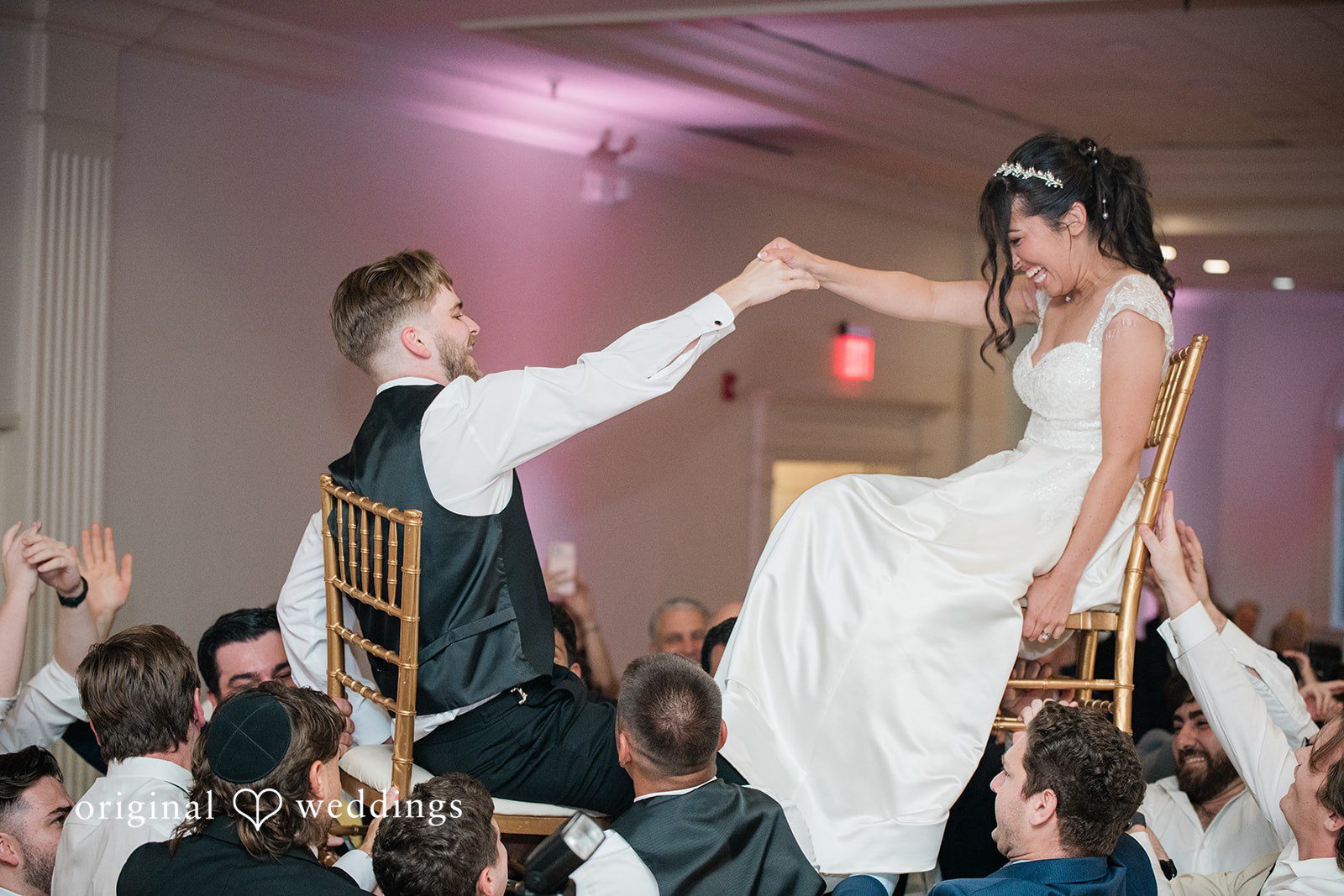 Julia + Camden A bride and groom are lifted into the air on chairs during a traditional reception dance.