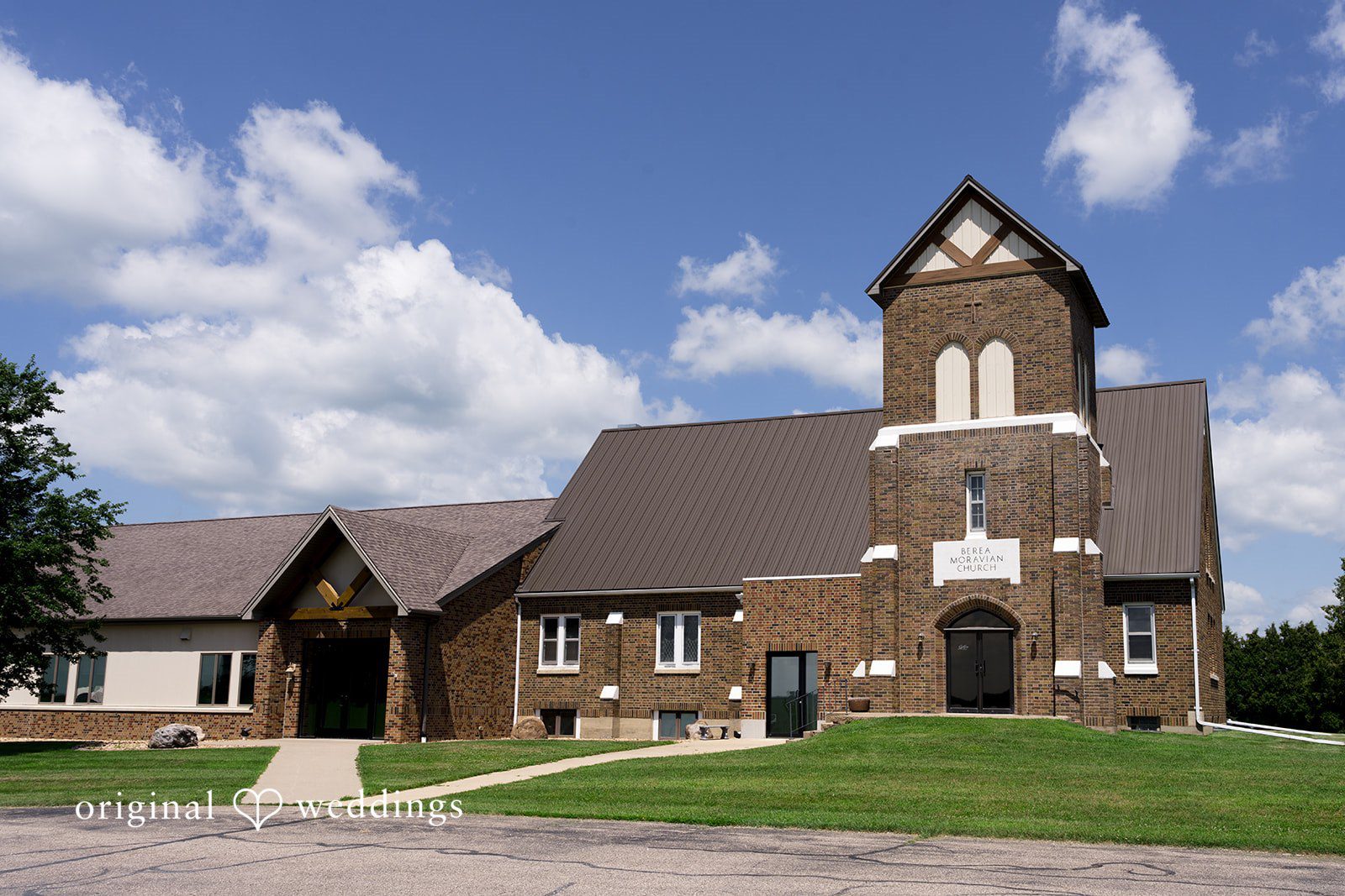 A quaint wooden church building with a tall steeple set against a bright blue sky.