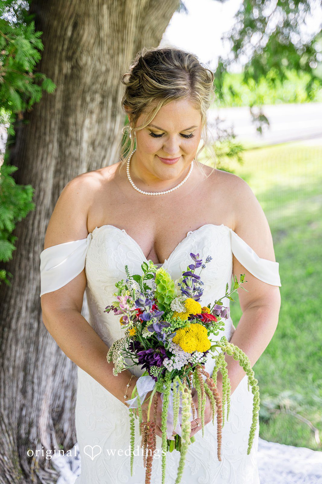 A smiling bride looking down lovingly at her vibrant bouquet of mixed flowers.