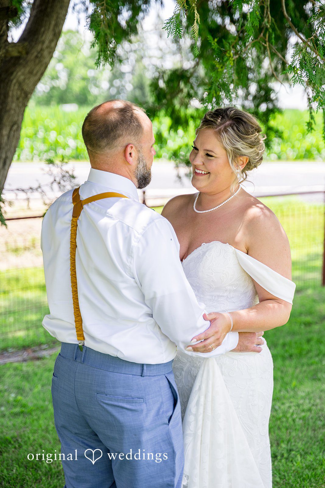 A bride and groom holding hands and smiling at each other on a sunny day.