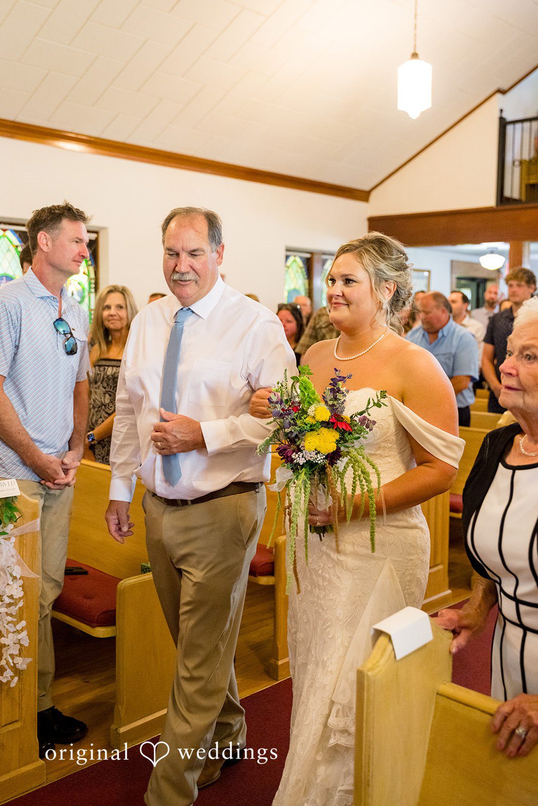 A bride and man in formal attire walking down an aisle together.