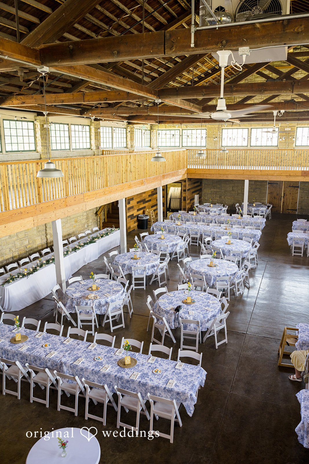 An expansive reception hall filled with neatly arranged white dining tables and chairs.