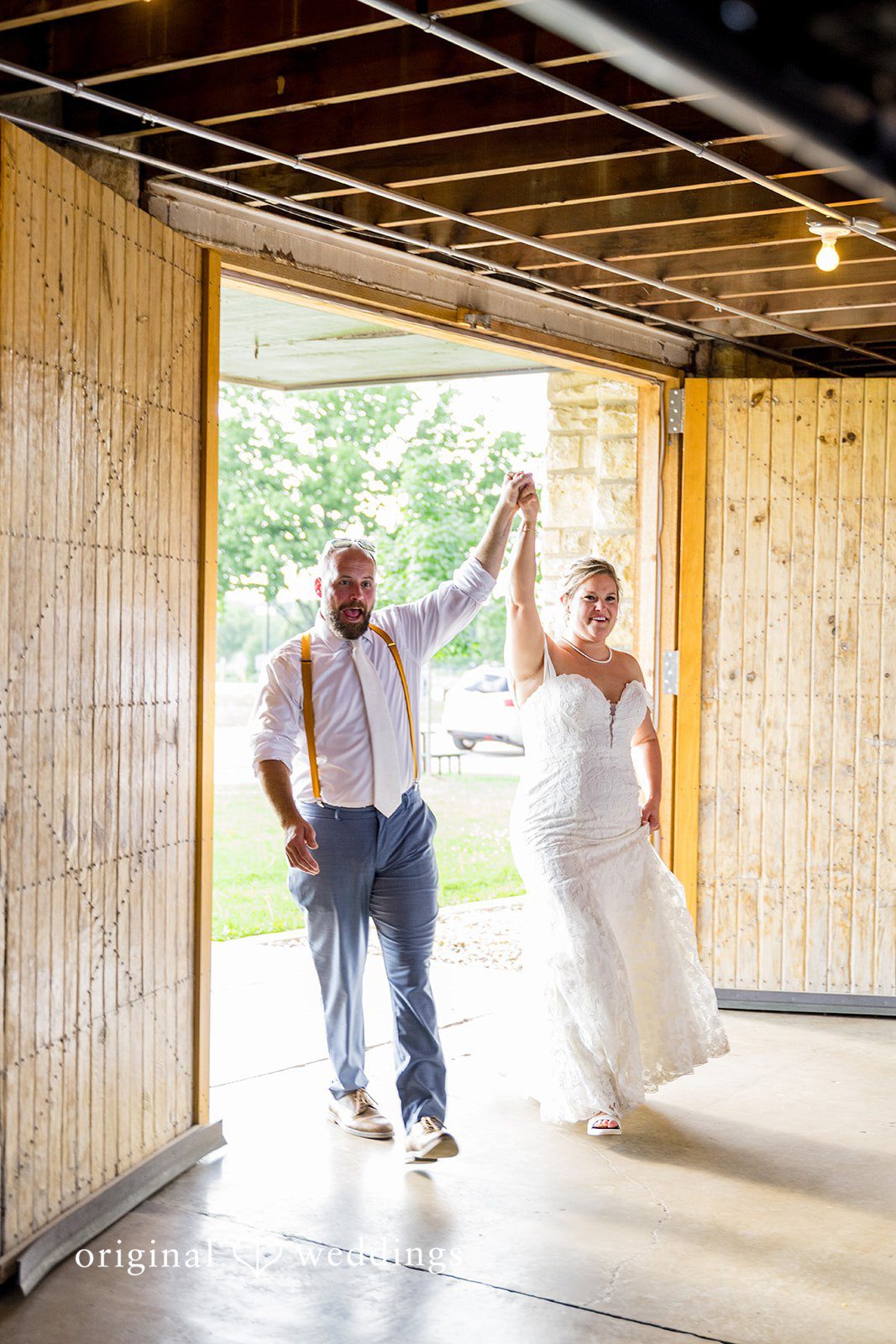 A bride and groom holding hands and walking together through the open doors of a rustic barn venue.