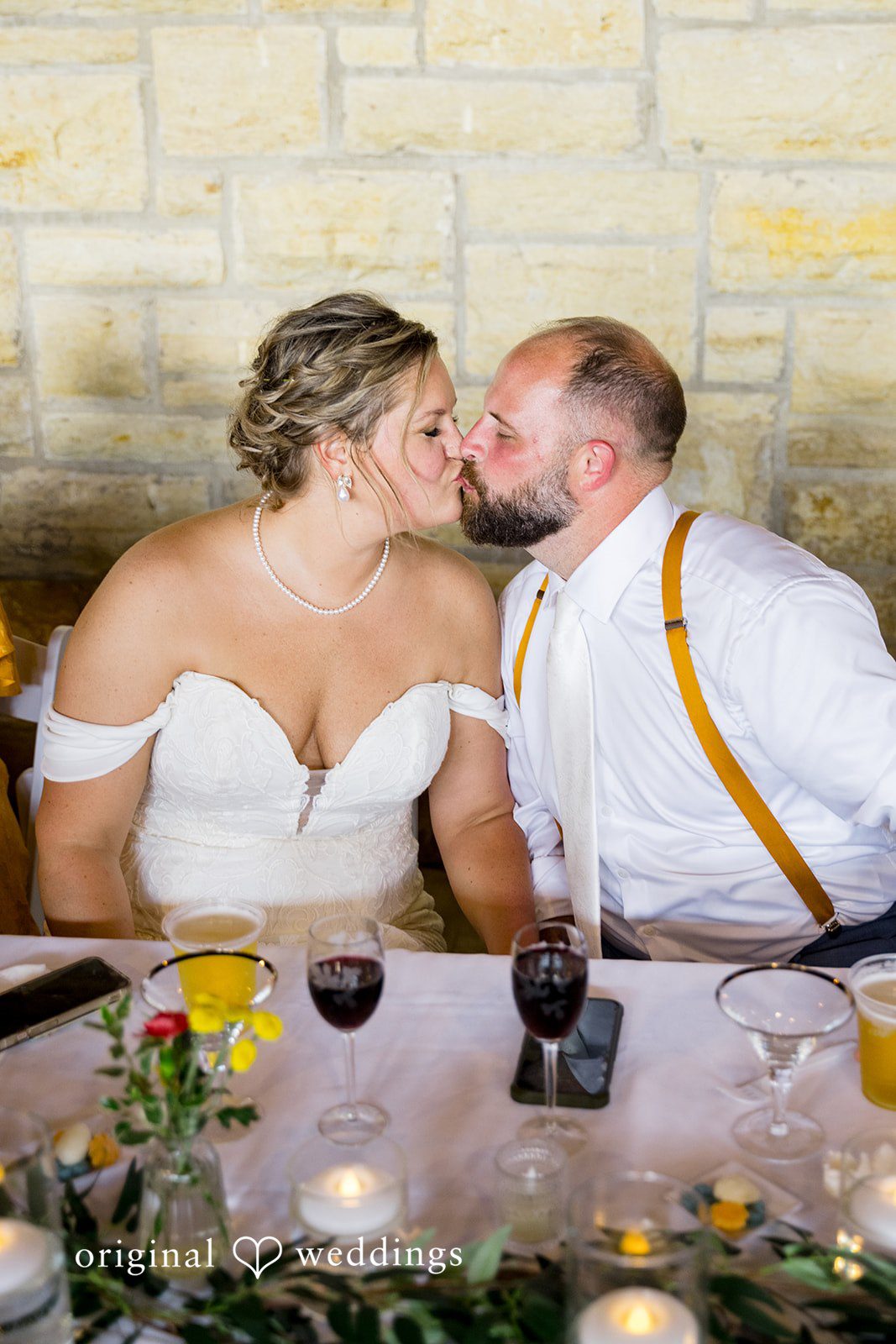 A bride and groom kissing across a decorated table during their wedding reception dinner.