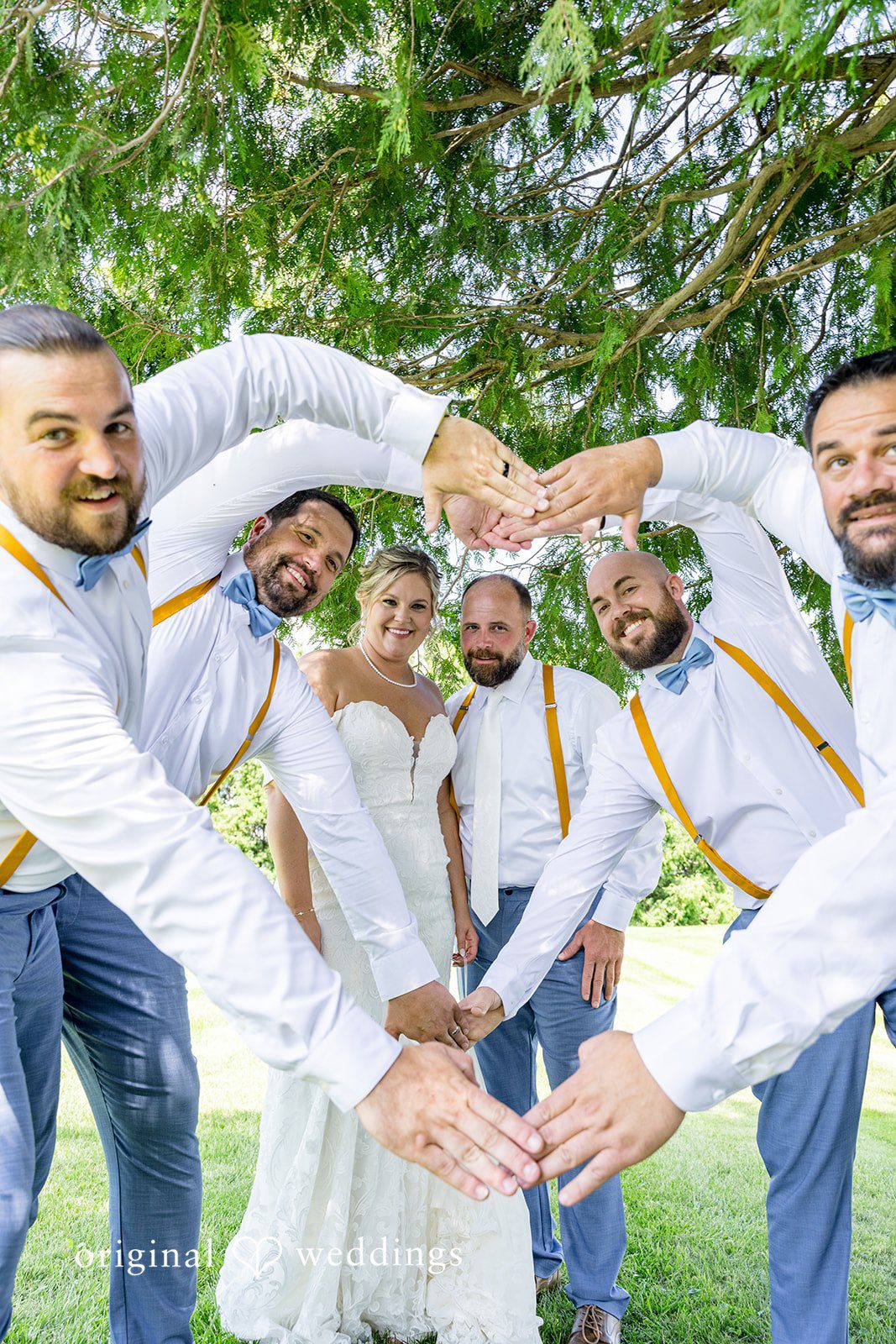 Groomsmen forming a circle with their hands over the bride and groom during a playful wedding photoshoot.